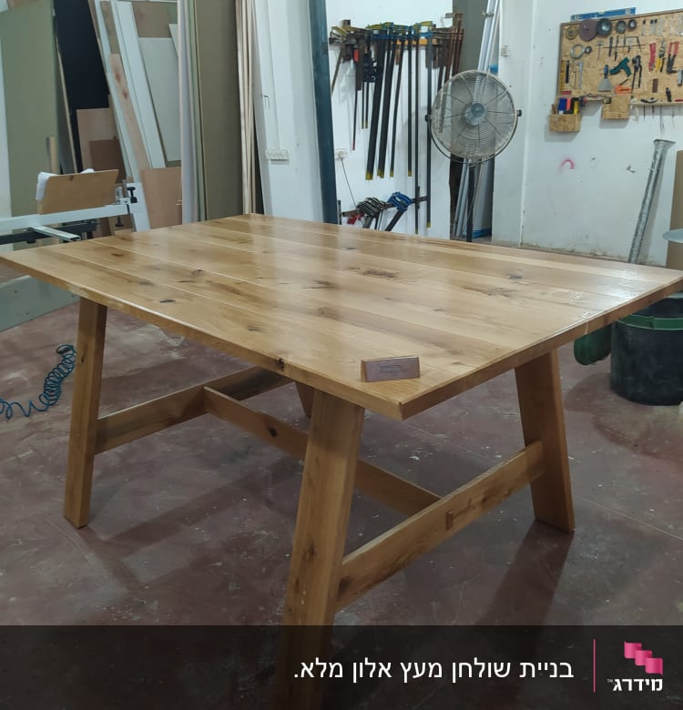 שולחן עץ גמור בסדנת נגרות עם כלים על הקיר